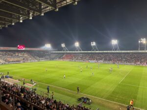 Wieczorny mecz na stadionie Cracovii w Krakowie — widok na boisko i trybuny.